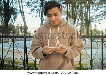happy latin man in brown clothes playing with cell phone in an outdoor park in la paz bolivia