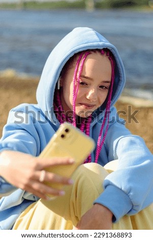 Happy caucasian teenage hipster girl with pink braids using a smartphone,taking selfies.Summer concept.Generation Z style.Social media concept.