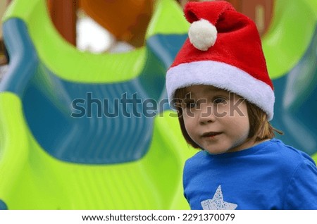 Portrait of a little boy in a Santa hat. The child on the playground rides from the children's slide. Concept: Christmas in kindergarten, winter holidays in the tropics. Warm winter