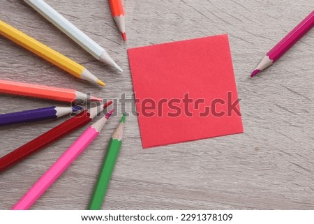 Red piece of paper on the wooden table with colorful pencils at the side. Copy space and message concept