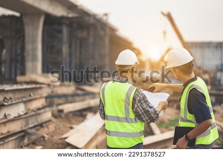 A team of civil engineers and architects wearing safety gear inspect the construction site of a high concrete bridge at a highway construction site. Royalty-Free Stock Photo #2291378527