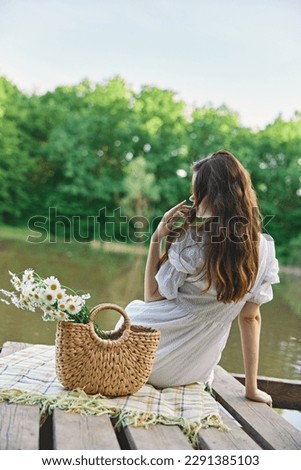 a woman with well-groomed hair is resting on the pier sitting with her back to the camera enjoying nature Royalty-Free Stock Photo #2291385103