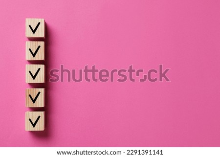 Wooden cubes with check marks on pink background, top view. Space for text