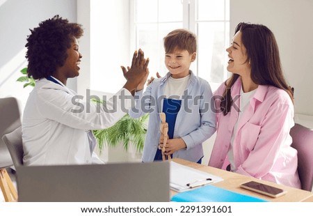 When seeing a doctor is fun. Cheerful pediatrician gives a five to a child patient. Joyful African American woman paediatrician high fives a happy little boy who came to the clinic with his mother Royalty-Free Stock Photo #2291391601