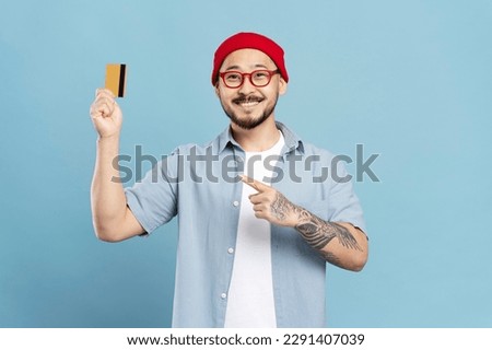 Portrait of handsome smiling Asian man wearing red, stylish hipster eyeglasses, holding credit card looking at camera isolated on blue background, successful business. Shopping, sales concept