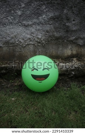 a green balloon with a smiling face placed in front of a gray cement wall