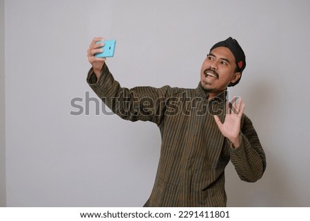 Asian man wearing javanese costume making selfie with his mobile phobe
