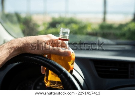 Driver driving a car with a bottle of alcohol in his hands close-up. Royalty-Free Stock Photo #2291417413