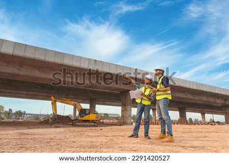 Asian architect and mature supervisors meeting at construction site Multiethnic workers and engineers discussing plans Two construction workers working together while visiting expressway construction Royalty-Free Stock Photo #2291420527