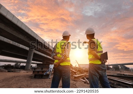 Asian architect and mature supervisors meeting at construction site Multiethnic workers and engineers discussing plans Two construction workers working together while visiting expressway construction Royalty-Free Stock Photo #2291420535