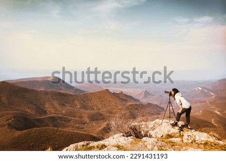 Young passionate attractive caucasian hipster woman content creator photographing mountains with red girly DSLR camera on tripod