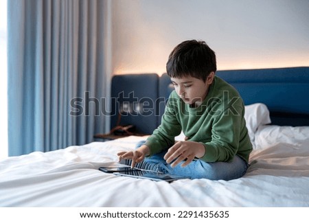 Kid boy using smartphone texting to friend,Child playing Game on Tablet while sitting on a bed. School kid using mobile phone for homework,Children with Technology ,Internet, Online Education concept