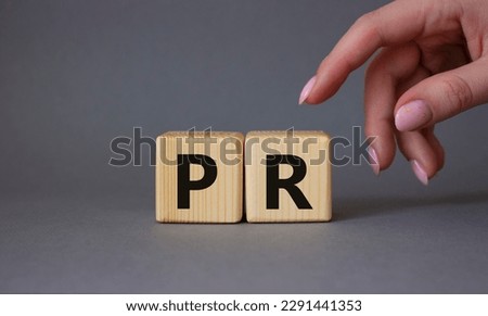 PR - Public Relations symbol. Concept word PR on wooden cubes. Businessman hand. Beautiful grey background. Business and PR concept. Copy space.