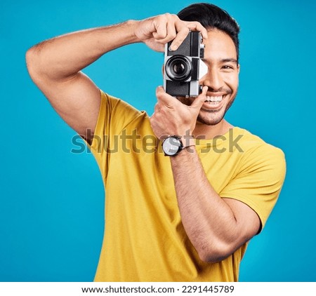 Happy, photographer and man with a camera in a studio for creative or artistic photoshoot. Photography, happiness and portrait of a male person with a hobby for memories isolated by a blue background