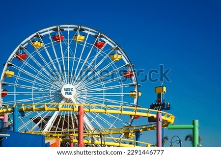 roller coaster, ferris wheel and a hammer in a colorful amusement park on a clear day with blue sky, a landscape from theme park in santa monica beach, los angeles, california, usa, november 2022