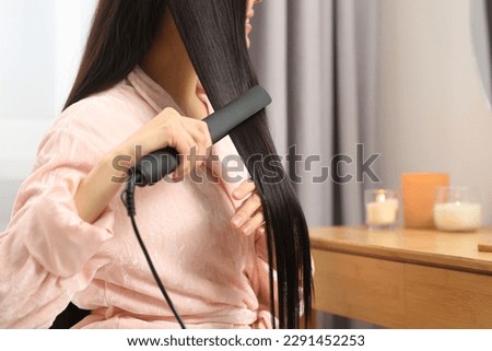 Woman using hair iron in room, closeup. Space for text Royalty-Free Stock Photo #2291452253
