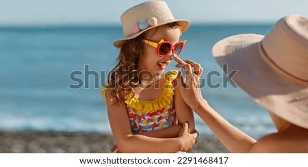 Mom carefully smears her child's face with protective cream on the beach Royalty-Free Stock Photo #2291468417