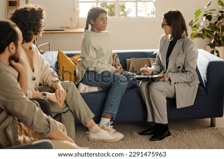 Social worker talking to teenage girl while they sitting on sofa in the living room with foster parents Royalty-Free Stock Photo #2291475963