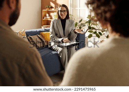 Young social worker in suit sitting on sofa in the living room and talking to foster parents about custody at meeting at home Royalty-Free Stock Photo #2291475965