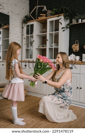 Happy birthday. Mom with daughter surprised. Kid congratulates mother and gives bouquet of tulip flowers in kitchen at home. Mother's Day concept. Greeting card. Women's Day. Back view. Family holiday