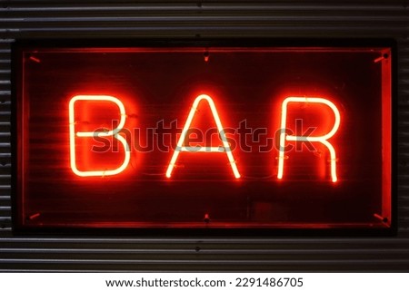 A bright red neon sign with the word bar in front of a striped metal wall at night. Luminous bar sign.