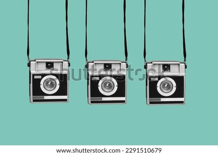 three gray and black retro film cameras, hanging from their straps, on a blue background