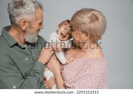 excited toddler girl laughing near happy grandparents isolated on grey Royalty-Free Stock Photo #2291552313