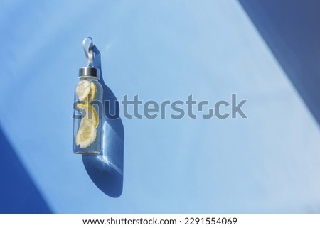 Lemon water drink detox in bottle, hard shadow at sunlight on blue background. Wellness, diet, eating healthy concept. Top view glass reusable water bottle, eco friendly lifestyle, minimal style photo Royalty-Free Stock Photo #2291554069