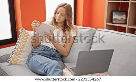 Young blonde woman using laptop writing on notebook at home