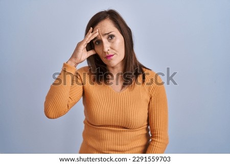 Middle age brunette woman standing wearing orange sweater worried and stressed about a problem with hand on forehead, nervous and anxious for crisis  Royalty-Free Stock Photo #2291559703