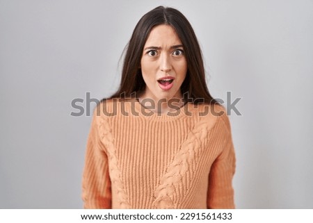 Young brunette woman standing over white background afraid and shocked with surprise and amazed expression, fear and excited face.  Royalty-Free Stock Photo #2291561433