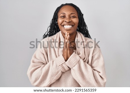 African woman standing over white background praying with hands together asking for forgiveness smiling confident.  Royalty-Free Stock Photo #2291565359