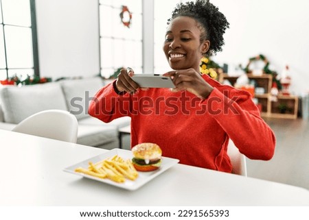 African american woman make photo by smartphone to hamburger sitting on table by christmas tree at home