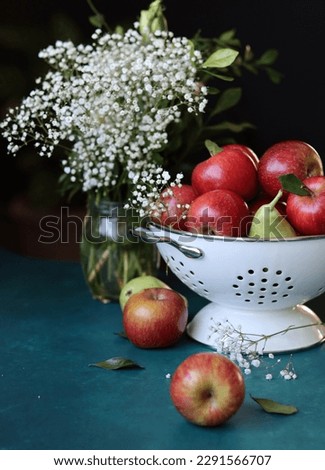 Red apples on black background. Vibrant colors of fresh seasonal fruit. Apples in a colander. White flowers and fruit still life. 