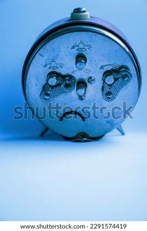 Blue overlay photo of a Red and white old fashioned rustic alarm clock on a white styrofoam background casting a light shadow on the left TBMNW11 87NHJUJB