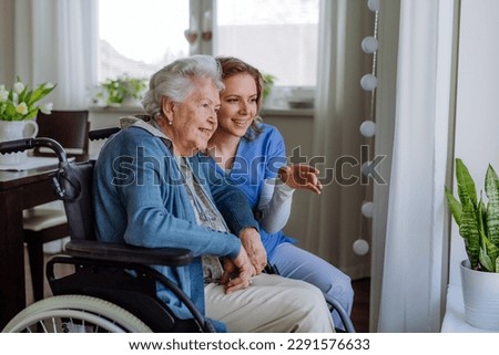 Portrait of nurse and her senior client on wheelchair looking out of window. Royalty-Free Stock Photo #2291576633