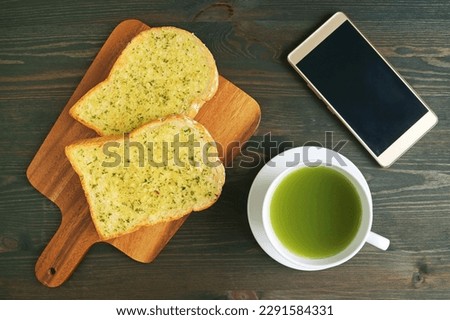 Top View of Garlic Butter Toasts with Hot Green Tea and Empty Screen Smartphone