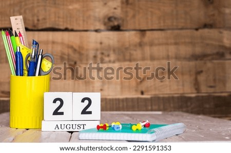 August calendar background with number  22. Stationery pens and pencils in a case on a wooden vintage background. Copy space notepad with pencils and calendar. Planner place for text. Royalty-Free Stock Photo #2291591353