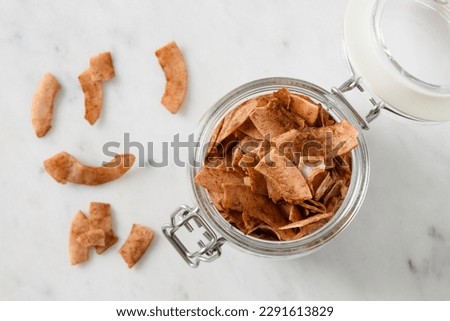 Coconut chips with cinnamon in glass jar on white background, home drying. Vegan and sugar free dessert. Copy space. Sri lankan local snack. View from above. Royalty-Free Stock Photo #2291613829