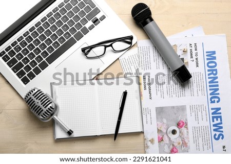 Laptop with eyeglasses, microphones, notebook and newspapers on light wooden background Royalty-Free Stock Photo #2291621041