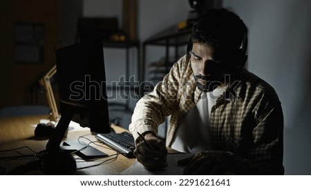 Young hispanic man business worker using computer and headphones writing on document at office