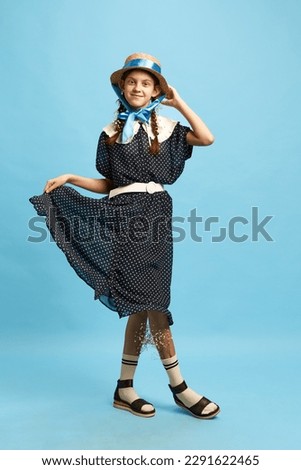 Little fashionista. One adorable little girl wearing old-fashioned clothes and holding her chiffon dress over blue background. Child fashion. Concept of modern fashion, uniqueness, art, model, ad
