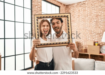 Young two people holding empty frame together celebrating crazy and amazed for success with open eyes screaming excited. 
