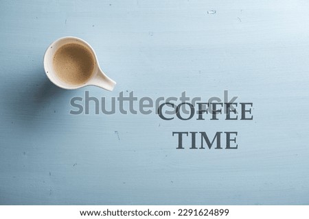 Top view of cup of fresh coffee placed over a simple plain light blue wooden background. Coffee time sign written next to it with black capital letters.