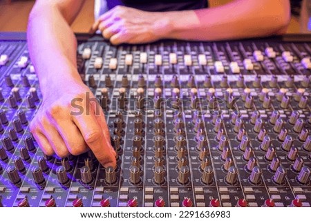 sound engineer hand tweaking EQ knob on audio mixing console in recording, broadcasting studio