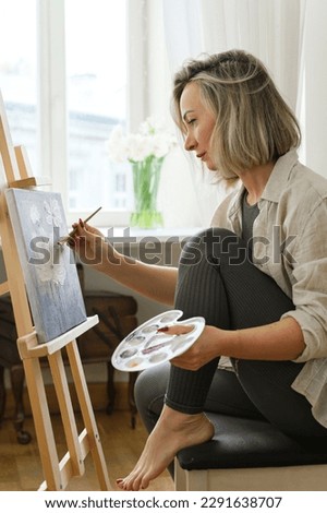 Young woman artist painting on canvas on the easel at home studio