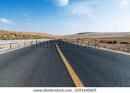 Empty asphalt highway road surrounded by fields with windmills Royalty-Free Stock Photo #2291640605
