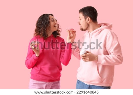 Young couple with tasty donuts and cup of coffee on pink background Royalty-Free Stock Photo #2291640845