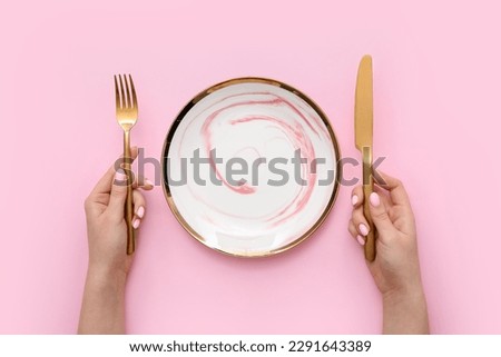 Woman with cutlery and empty plate on pink background Royalty-Free Stock Photo #2291643389