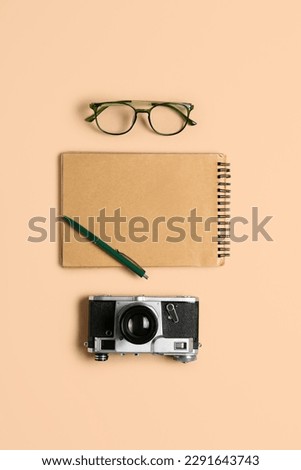 Notebook with pen, photo camera and eyeglasses on beige background
